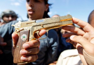 Ливиялық жас жігіт Каддафидың тұрағынан оның алтын жанқұралын тауып алып журналистерге көрсетуде